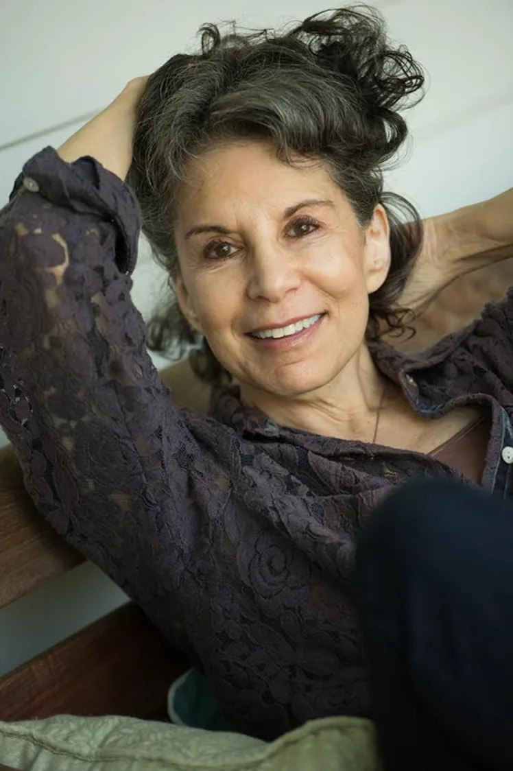 Woman smiling while reclining with hands behind her head, wearing a lace top