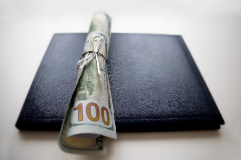 Rolled-up 100-dollar bill tied with string, placed on top of a closed black book