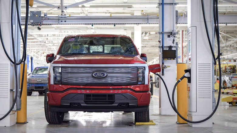 A red Ford F-150 Lightning plugged in at a charger in a warehouse