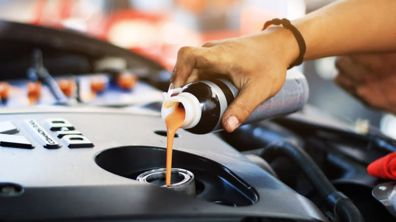 A person pouring engine oil additive into motor.