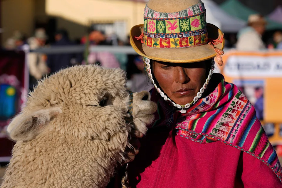 A woman in traditional clothing stands beside a llama.