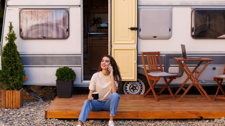 Young woman talking on phone in front of travel trailer