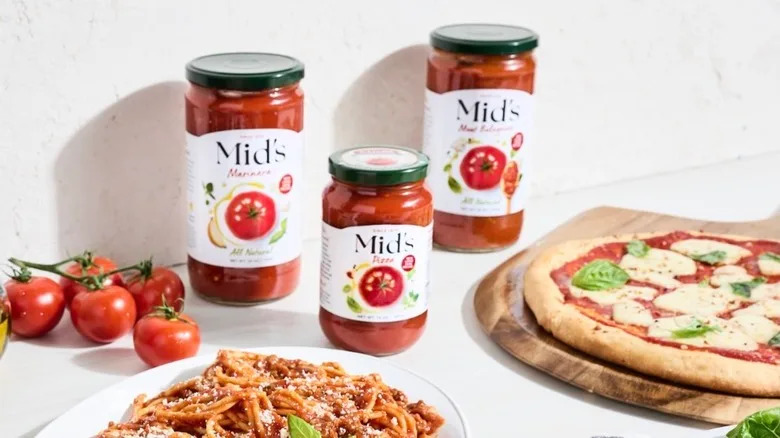 Jars of Mid's sauce with pizza, pasta, and tomatoes