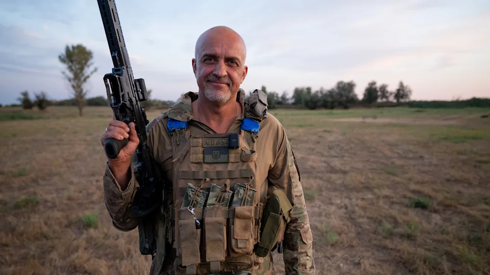 Ihor "The Knifer" stands with his gun aloft and a smile on his face in his uniform