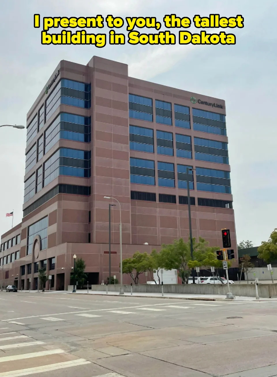 A short modern office building with "CenturyLink" signage, seen from across an empty street corner. Caption: "I present to you, the tallest building in South Dakota"