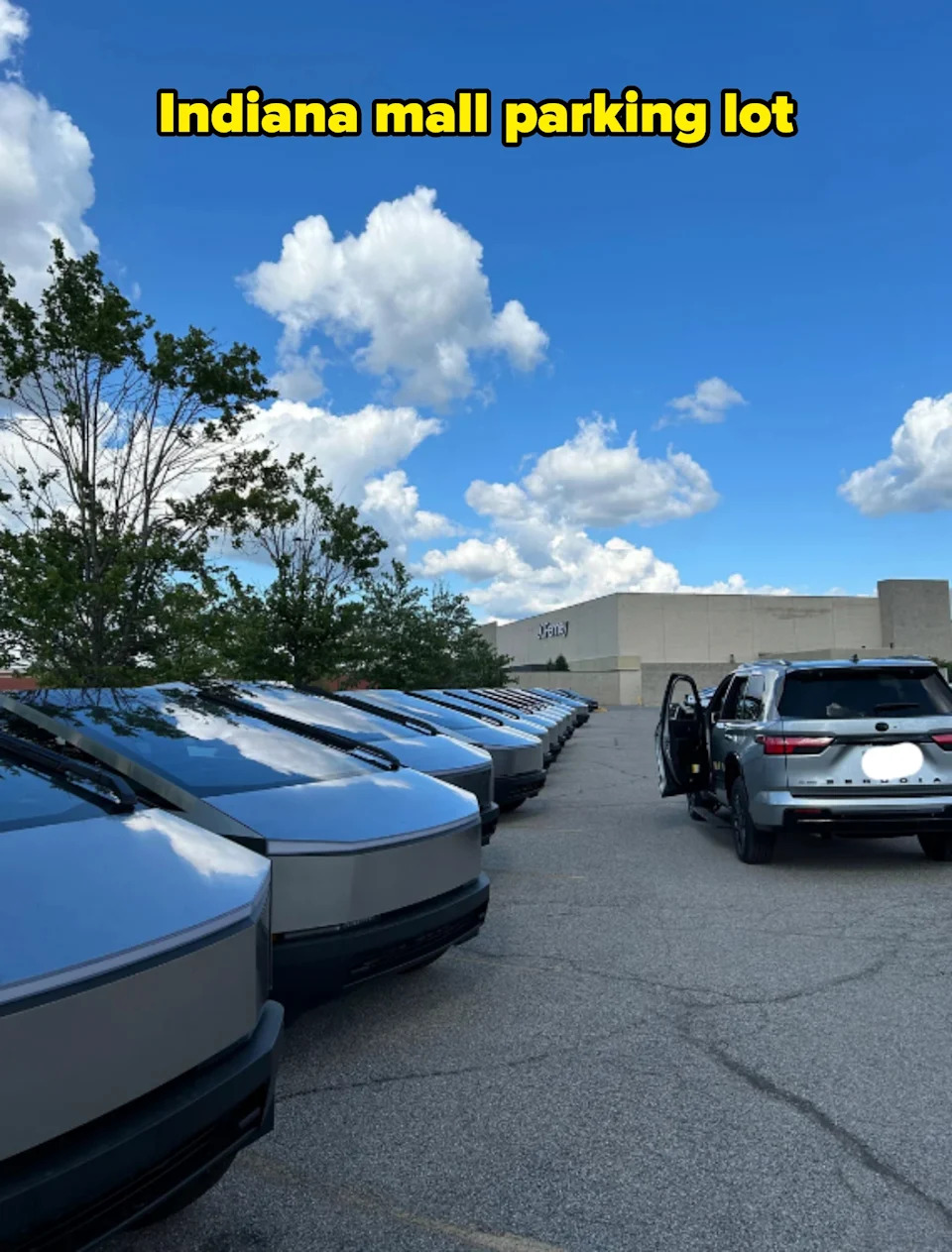 Line of futuristic cars parked in a lot under a blue, cloudy sky at a mall. People exit a parked SUV nearby
