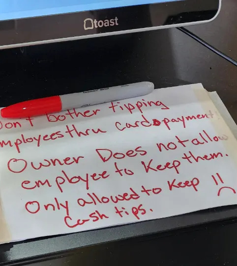 Note on paper saying employees can't keep credit card tips, only cash, with a sad face
