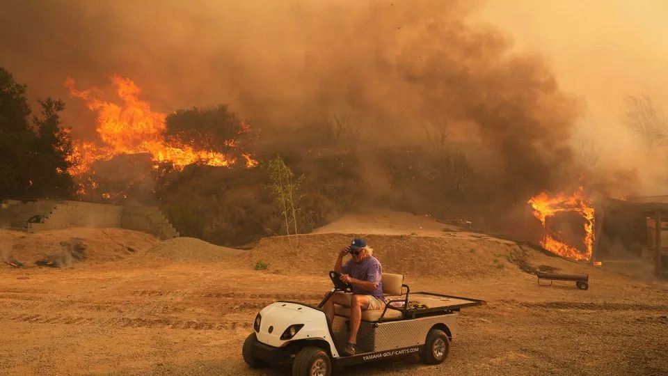 A resident rides a golf cart as he exits his property while the Canyon Fire burns on Thursday in Halsey Canyon, California. - Marcio Jose Sanchez/AP