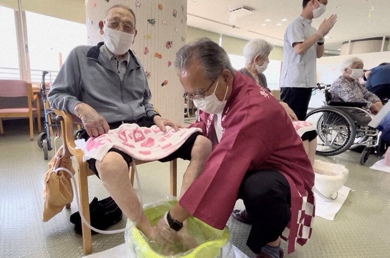 源泉の足湯につかる「倉掛のぞみ園」の入園者（左）と湯村温泉観光協会の西村一彦副会長（手前）＝広島市安佐北区で2025年7月30日（兵庫県新温泉町提供）