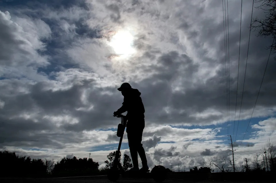 A pedestrian rides an electric scooter down the Calaveras River Bike Path under a canopy of cloudy skies in Stockton, Calif. on Feb, 6. 2024.