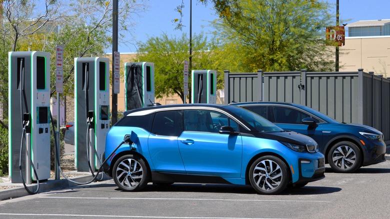 A metallic blue BMW I3 electric car parked at an Electrify America charging station at a commercial business location.