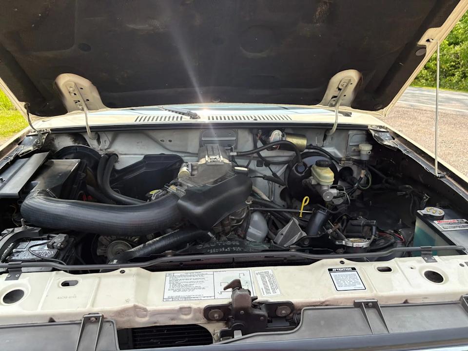 engine bay view showing black hoses, battery, and various engine components under open hood.