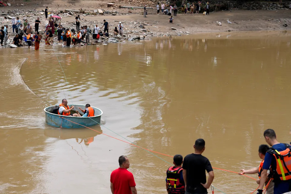 Rescuers pull on a rope, towing people across a flooded river in a round plastic basin.