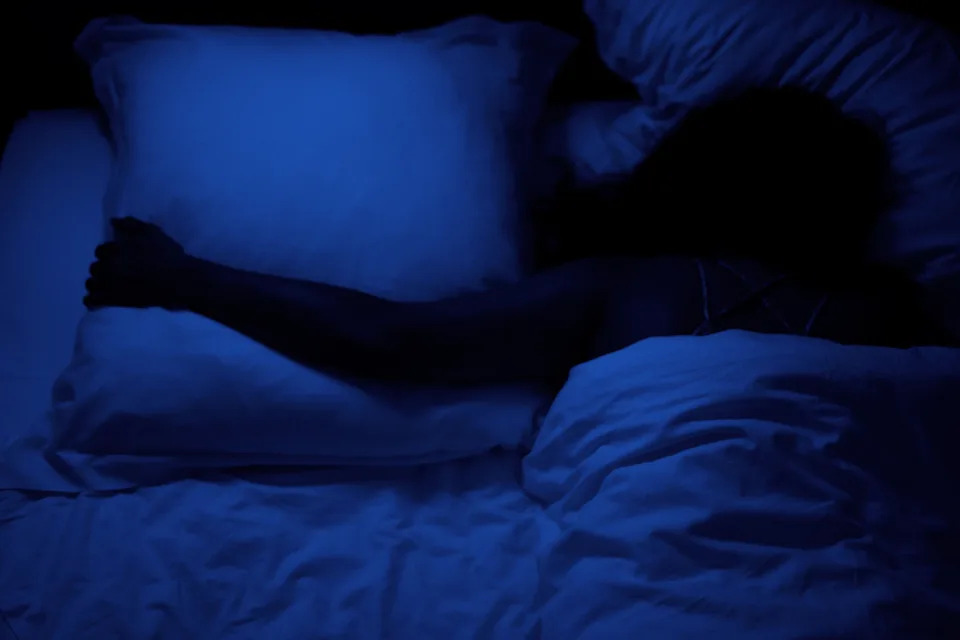 Person sleeping in a bed at night, hugging a pillow. The scene conveys rest and relaxation, related to work-life balance