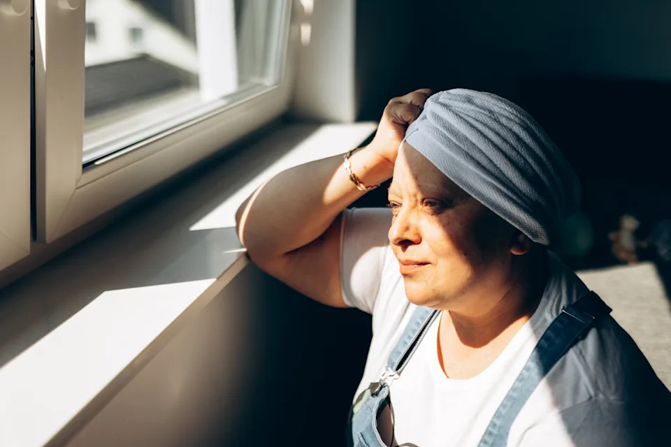 Person in a headwrap and overalls gazes out a window, appearing contemplative