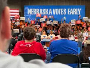 Ruth and Jason Huebner-Brown pump up a crowd of Democrats talking about the history of their “blue dot” signs and tee shirts in 2024. (Aaron Sanderford/Nebraska Examiner)
