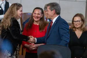  Gov. Jim Pillen, right, shakes hands with State Sen. Wendy DeBoer of Omaha as State Sen. Danielle Conrad of Lincoln smiles at the pair. First Lady Suzanne Pillen looks from the right. Jan. 15, 2025. (Zach Wendling/Nebraska Examiner)