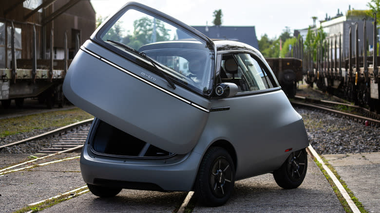 a matte black Microlino with its door open parked on train tracks