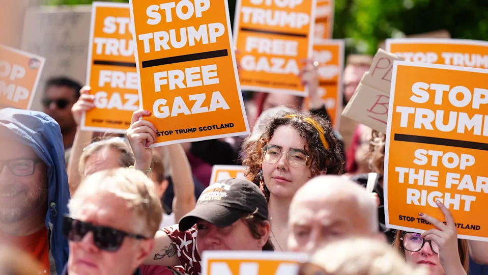 A crowd of anti-Trump protesters with orange signs bearing slogans including "Stop Trump Free Gaza"