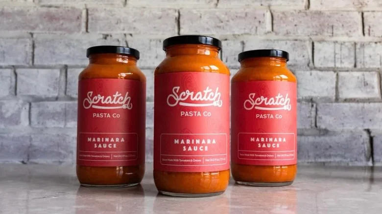 Jars of Scratch Pasta Co. marinara lined up in front of a brick wall