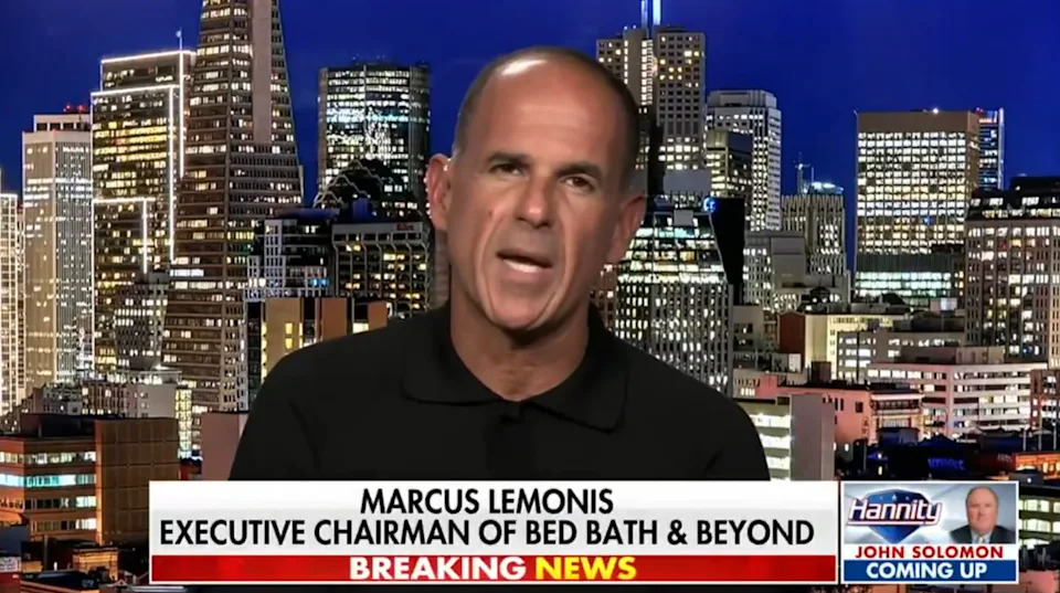 Man in a studio discussing news, with cityscape backdrop. Caption reads: "Marcus Lemonis, Executive Chairman of Bed Bath & Beyond."