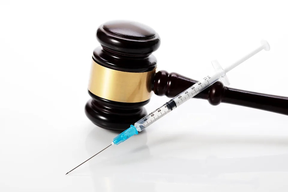 A syringe leaning against a gavel on a white background