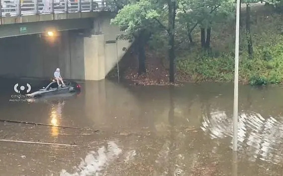 A person sits on top of a car submerged in water