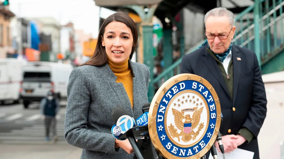 AOC at lectern; Sen. Schumer looks on from her left