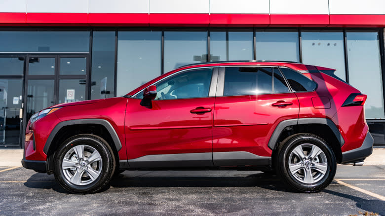 A side profile of a red Toyota RAV4 at a dealership