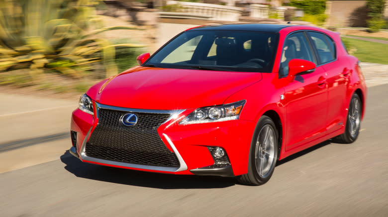 a red Lexus CT200h driving past homes