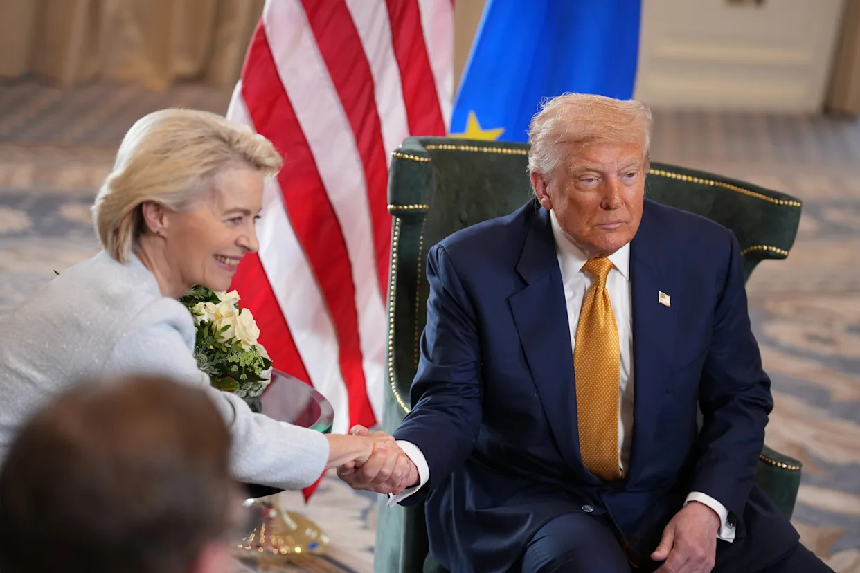 Trump shakes hands with Ursula von der Leyen, with the US and EU flags behind them.