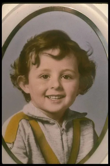 Child smiling in an oval portrait, wearing a light-colored jacket with dark highlights