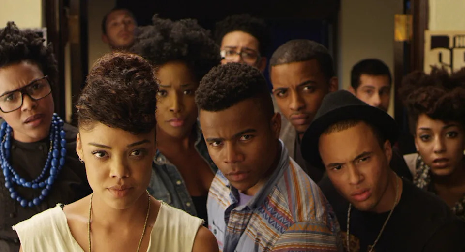A group of young adults with varied hairstyles and expressions stand together, all looking intently forward