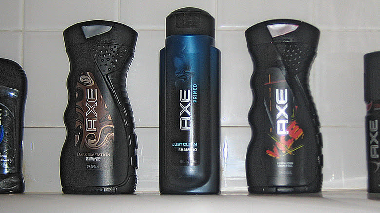 A lineup of Axe body wash, shampoo, shower gel, and deodorant in front of white bathroom tile