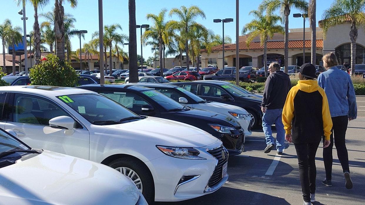 A parent and his teenagers looking at a row of used cars. - Simone Hogan // Shutterstock