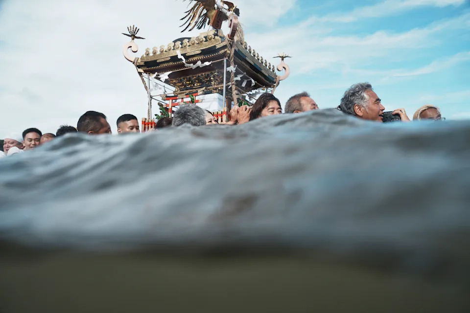 Worshippers carry a portable shrine into the sea, seen from the water's surface.