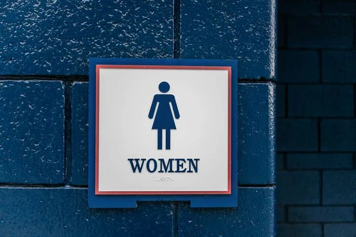 Women's restroom sign on a blue brick wall displaying a stylized figure in a dress
