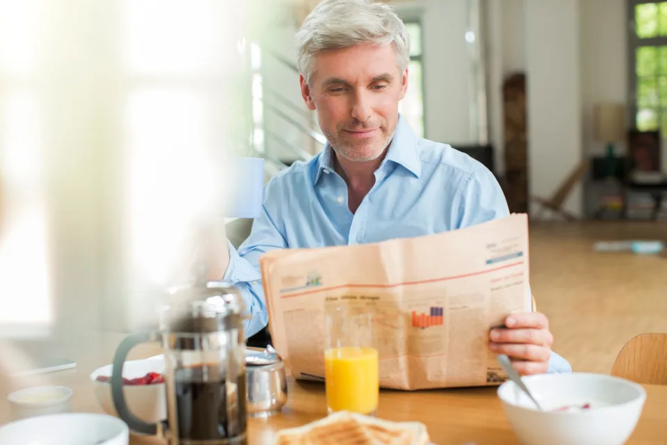 Older man reading newspaper over breakfast.