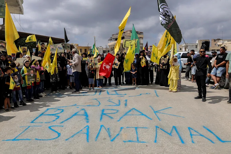 Protestors hold up Hezbollah flags behind graffiti reading