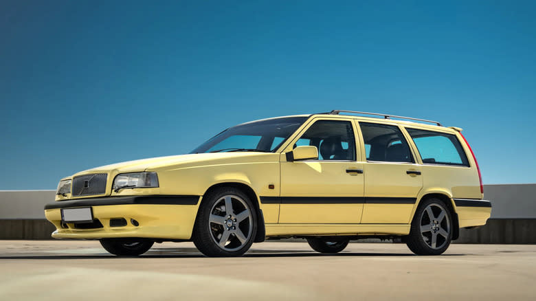 A yellow 1995 Volvo 850 R wagon parked in front of a short wall