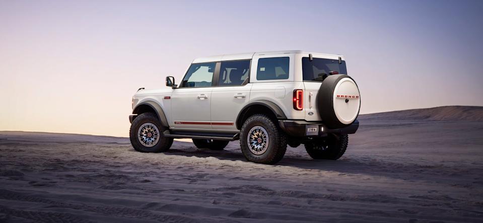 rear left angle of white suv parked on sand with spare tire mounted on tailgate.