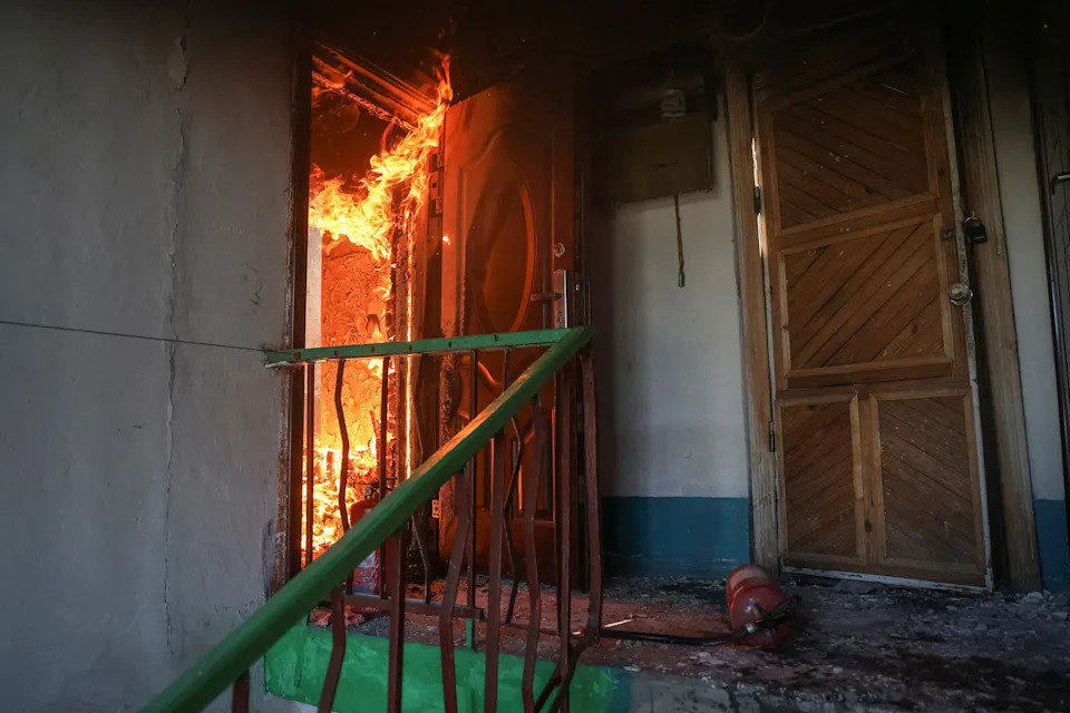 A fire burns inside a residence, seen through an open door.