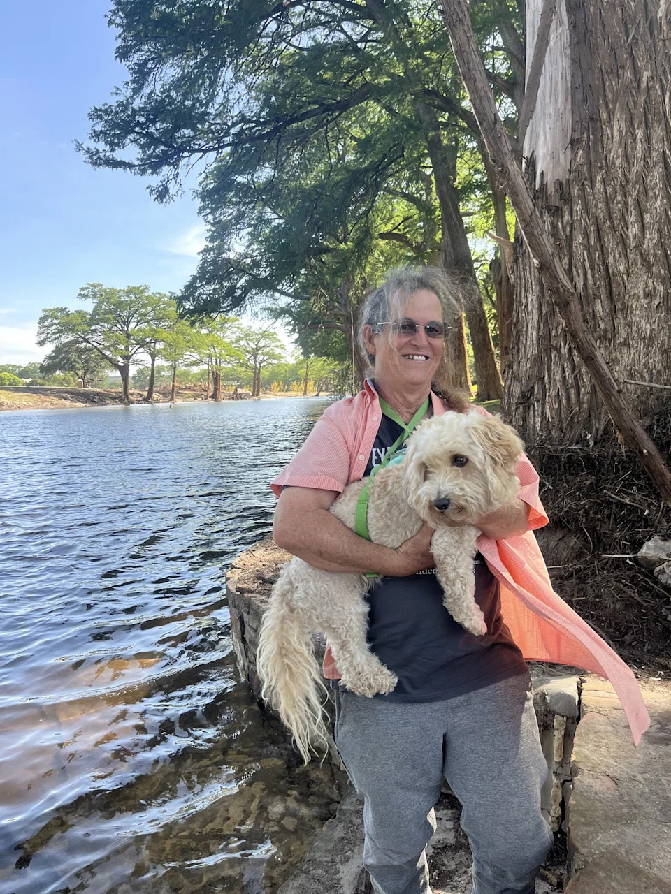 a man holds his whit dog near a river