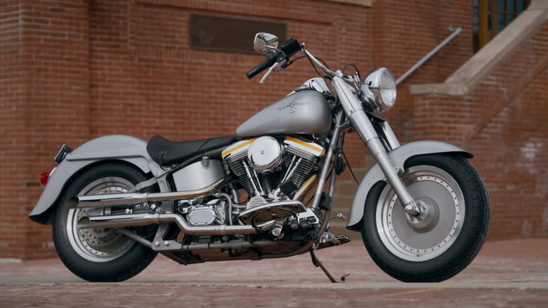 A silver Harley-Davidson Fat Boy parked next to a brick wall