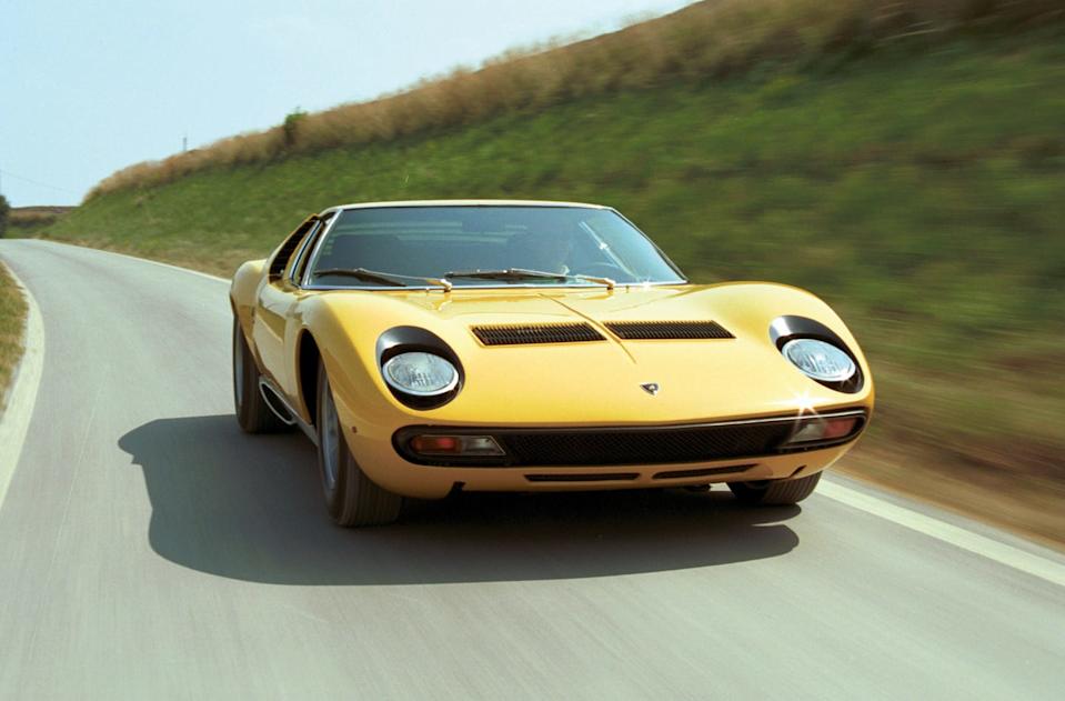 lamborghini miura driving down a road on a sunny day