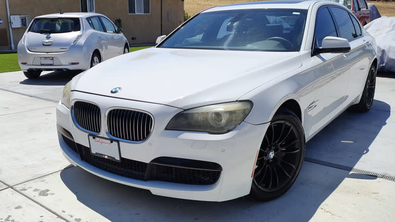 a white 2011 BMW 750Li sedan parked in a parking area, with a Nissan in the background.