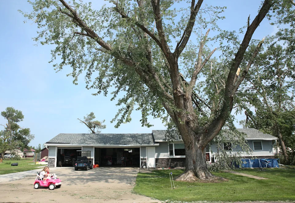 Neighborhood children play in a driveway as volunteers help clean up tree debris in Hudson on Tuesday, July 29, 2025 after severe weather moved through the area Monday evening. The system damaged trees, homes and other structures. (Makenzie Huber/South Dakota Searchlight)