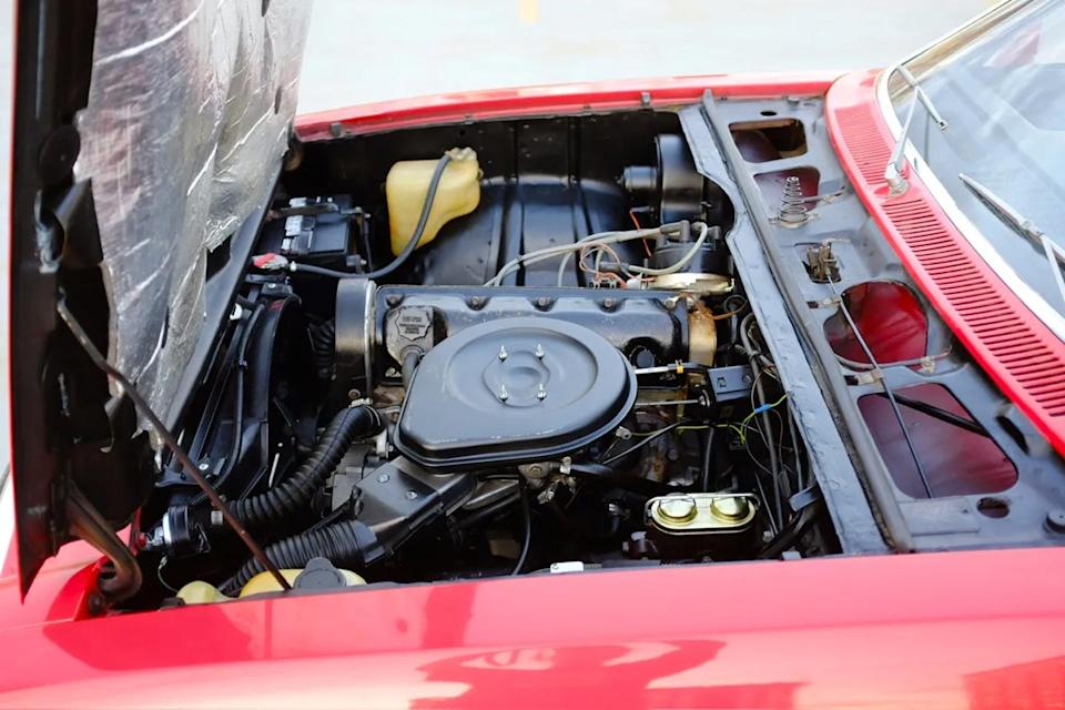 engine bay view with open hood showing black air cleaner, wiring, and fluid reservoirs on red body frame.