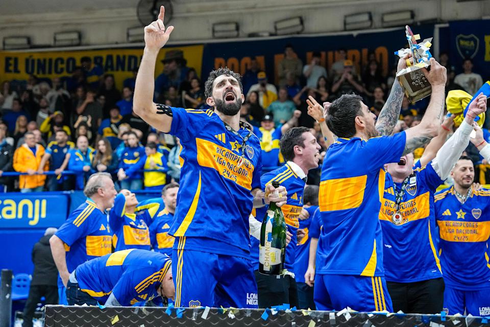 Sebastián Vega celebra la copa con su brazo derecho en alto, mientras que con su mano izquierda sostiene una botella de champaña, rodeado de sus compañeros