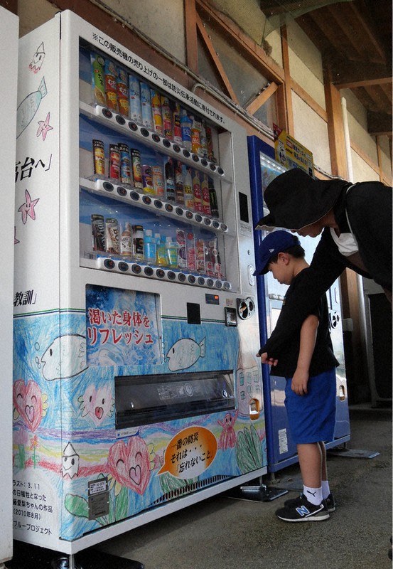 佐藤愛梨ちゃんの絵でラッピングされた自販機に見入る来場者ら＝熊本県氷川町大野の道の駅竜北で2025年8月5日午後0時12分、中村敦茂撮影